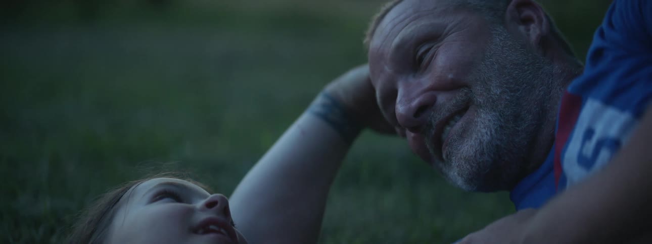 A father and daughter laugh and lay in the grass