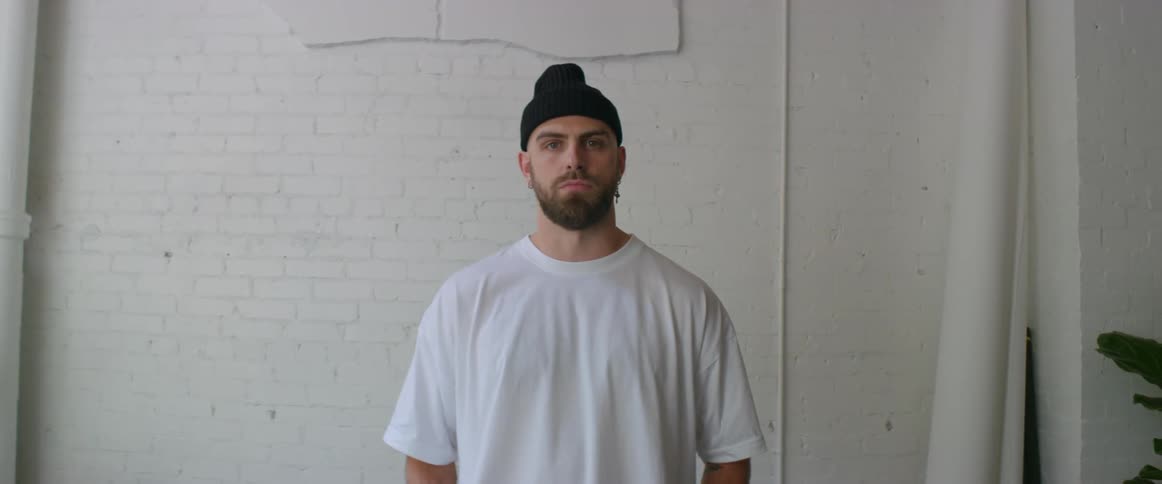 Man wearing a black beanie and white shirt standing in front of a brick wall