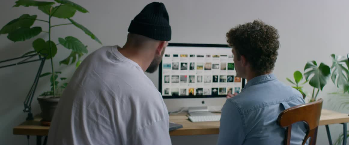 Two young men sitting in an office in front of a computer selecting images on the screen
