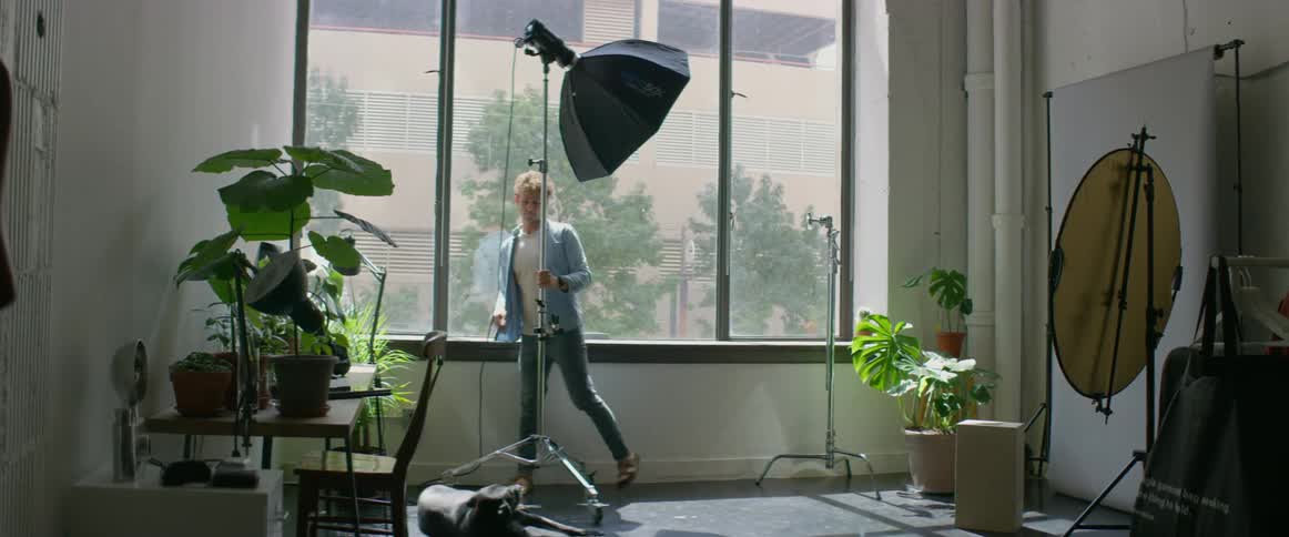 A man in a room moving a spotlight with a wall and window in the background
