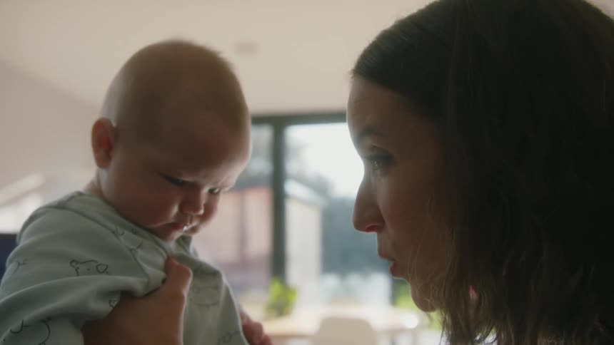 A woman makes kissy faces while holding her son up