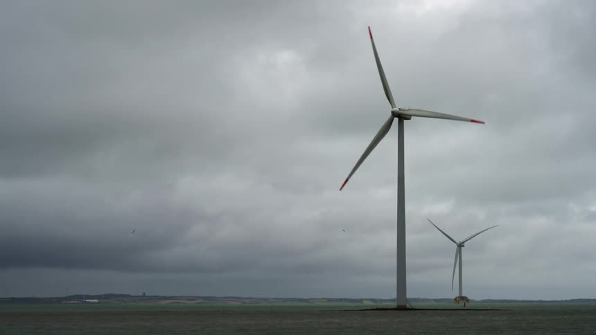 Wind turbines spin on a wind farm under a cloudy sky