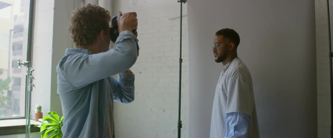 Photographer takes pictures of a model in front of a white backing in an apartment