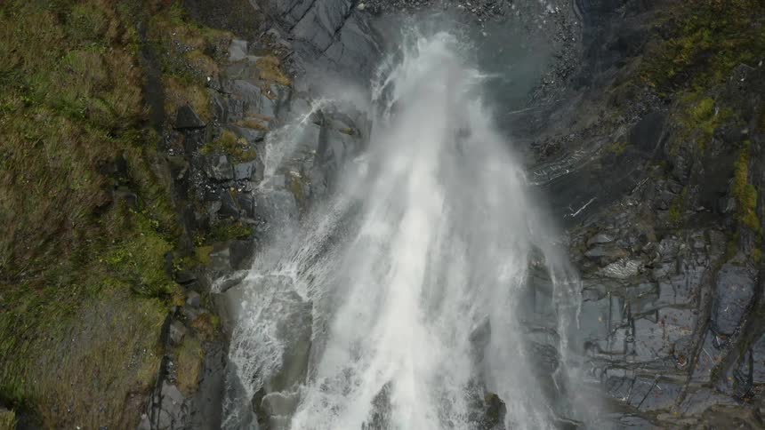 Aerial top down view of a waterfall over a rocky cliff in the mountains
