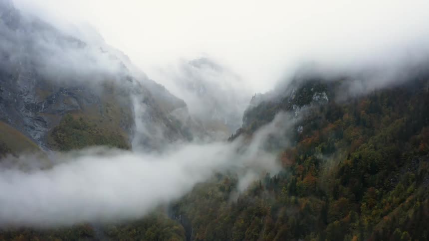 An aerial view of a valley between forested mountains on a foggy day with low clouds during the fall season