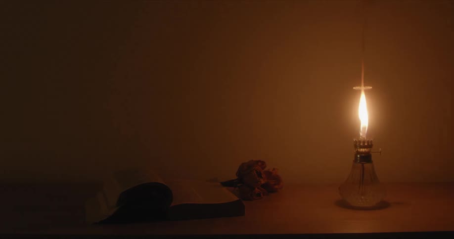 An old oil lamp is burning on the desk near the book