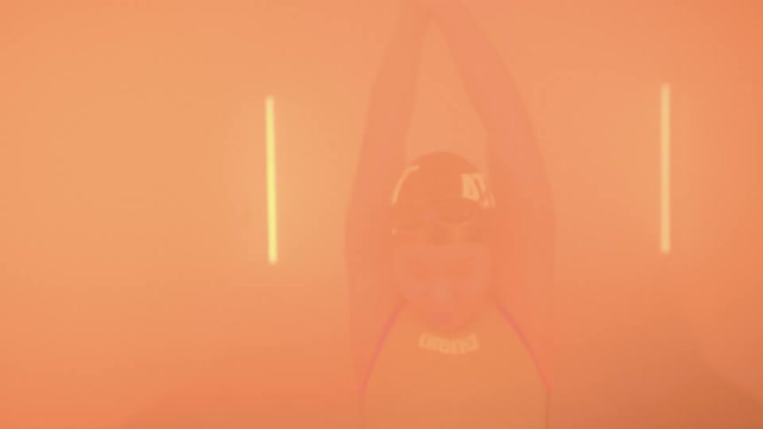 Young woman wearing swimming gear stretches and jumps inside a room with strobing orange lights