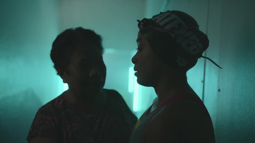 Woman arrives to encourage female swimmer waiting in corridor lit by neon lights