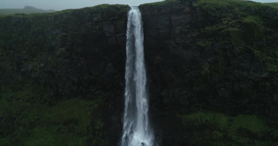 Birds are flying around waterfalls falling over a grass covered cliff