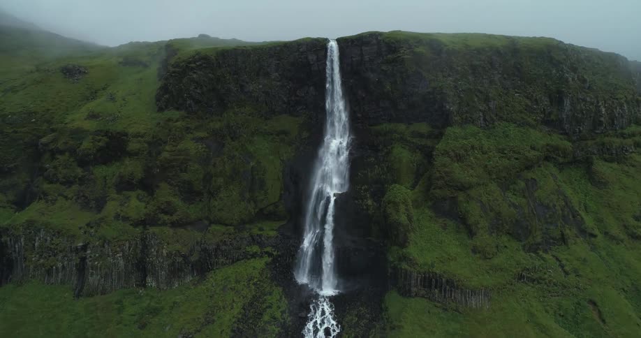 A waterfall plunges down a plant covered canyon