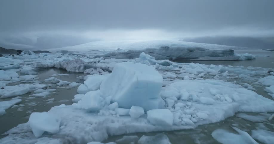 Aerial footage of an arctic region with chunks of ice in freezing water on a cloudy day