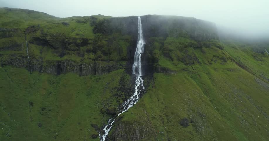 A cliff with a waterfall and river with the sky and clouds in the background