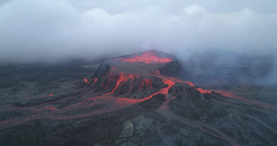 Molten lava spills from the top of a volcano during the day