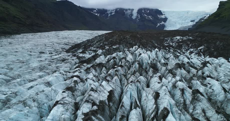 Ice and snow cover rough terrain of valley between dark mountains and glacier
