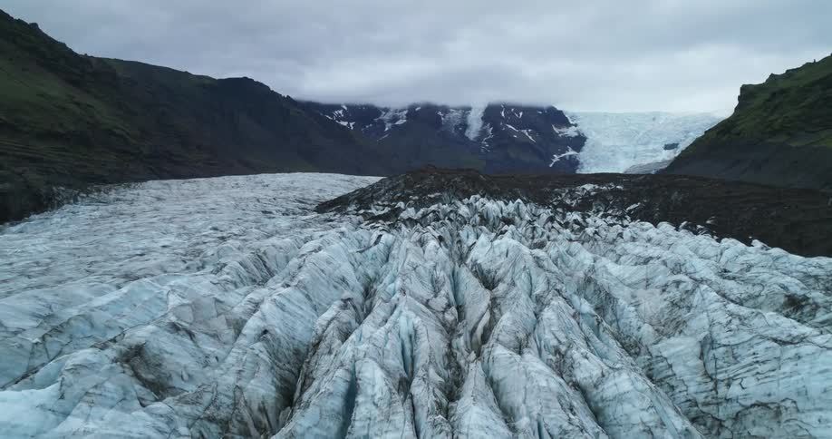 An aerial view of a glacier in a mountain region on a cloudy day