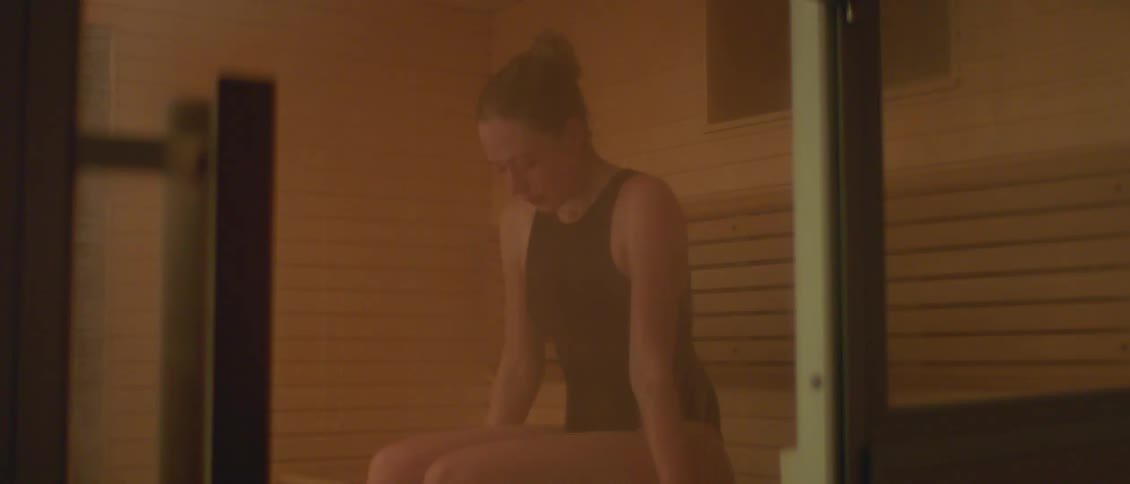 A woman sitting on a bench in a sauna takes a deep breath and lifts her head