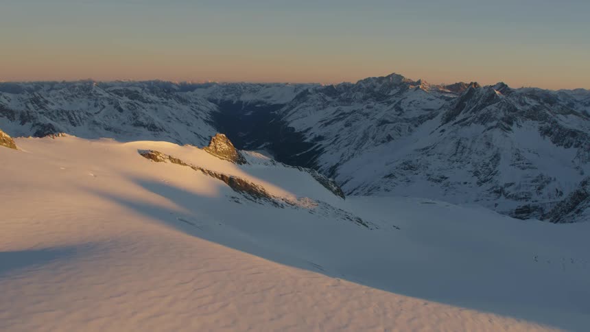 Sun casts valley snow covered valley and mountains into shadow under a red sky