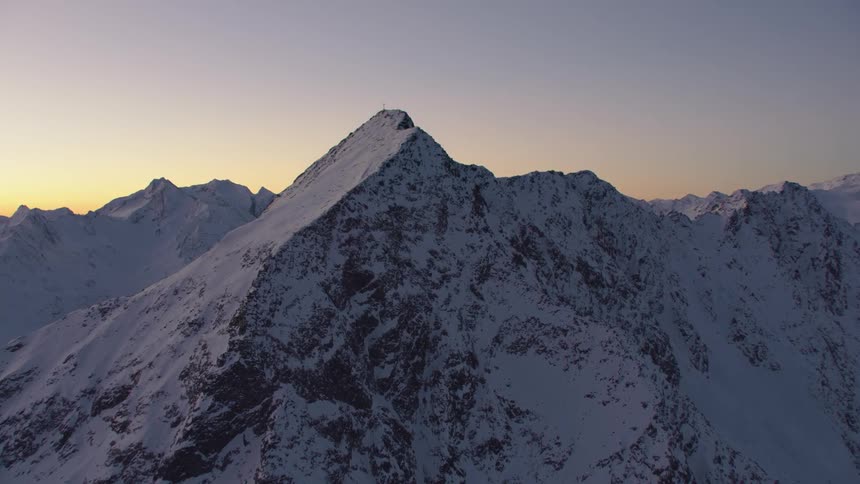 Cross sits on snow covered mountain summit against a clear red tinted sky
