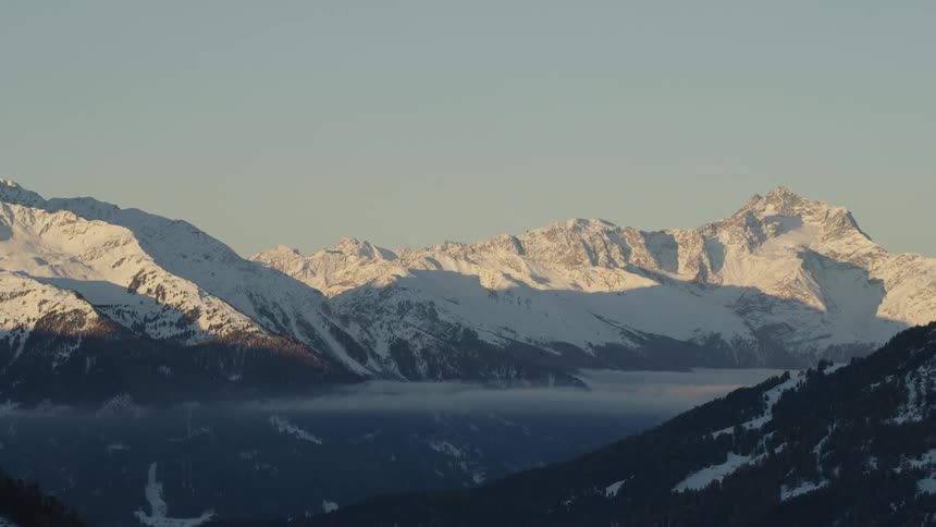 The sun is shining on snow covered mountains high in a clear sky