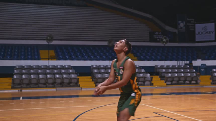 Athlete practices with volleyball standing on basketball court in middle of stadium