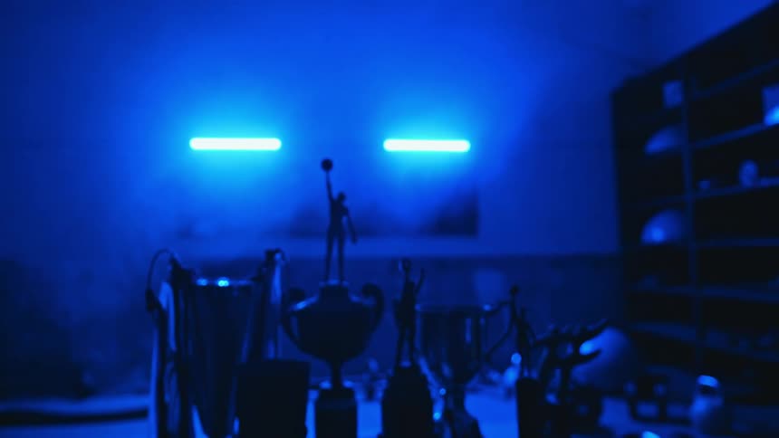 Sports trophies line a table in a room lit up with blue lights