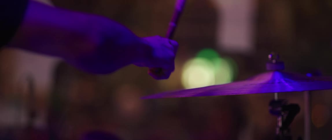 Hand of a drummer hitting a cymbal with a drumstick under blue and purple lights