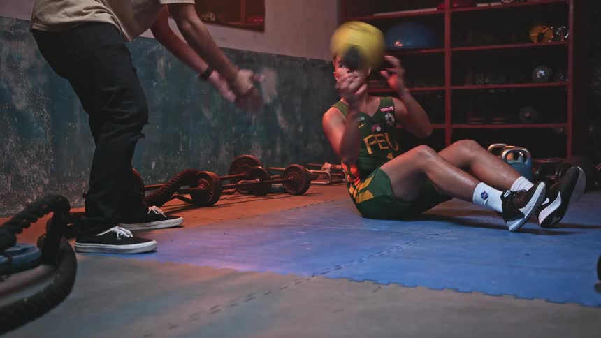 A trainer is passing a volleyball back and forth with a young man who is sitting on a mat