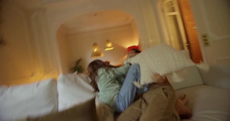 Brother and sister having a pillow fight over a couch in the living room