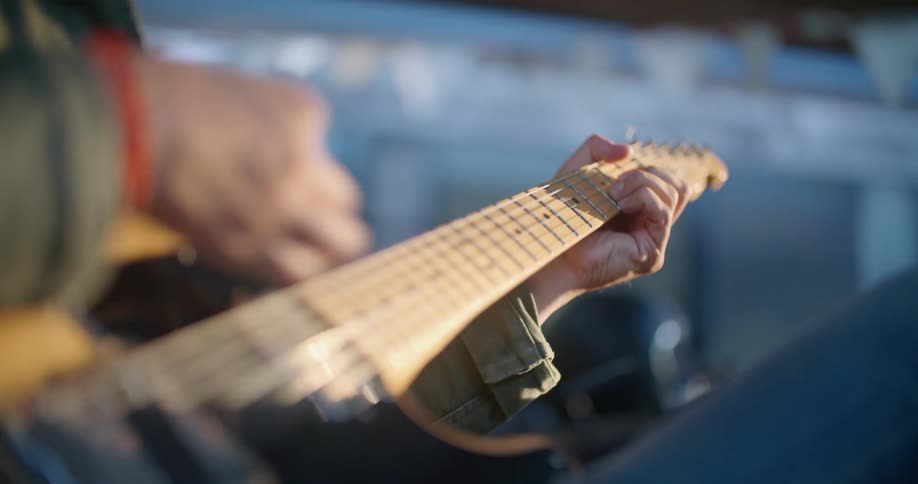 Man wearing jacket sits and plays guitar