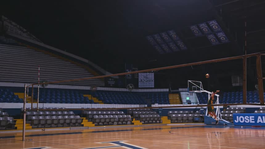 Volleyball player practices ball throws over the net inside a stadium