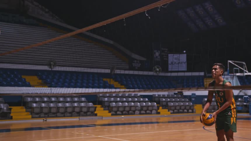 Young man practicing volleyball against a net inside the stadium