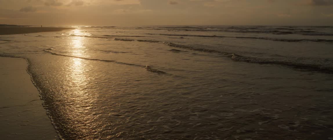 Aerial view of gentle ocean waves washing the shores on a beach at sunset