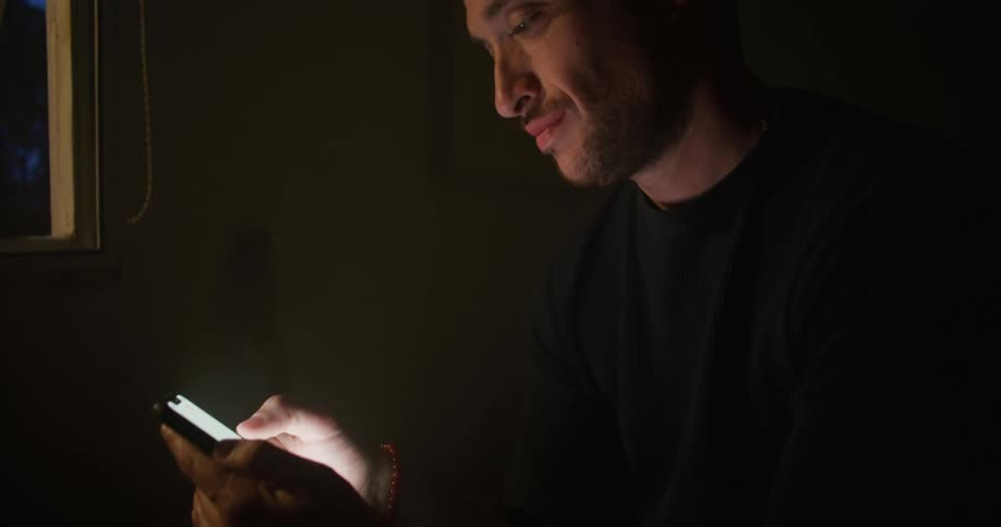 Man sits smiling while texting at night