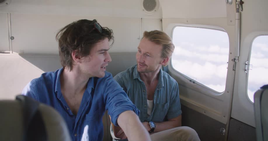Two men talk and point around while riding in a plane