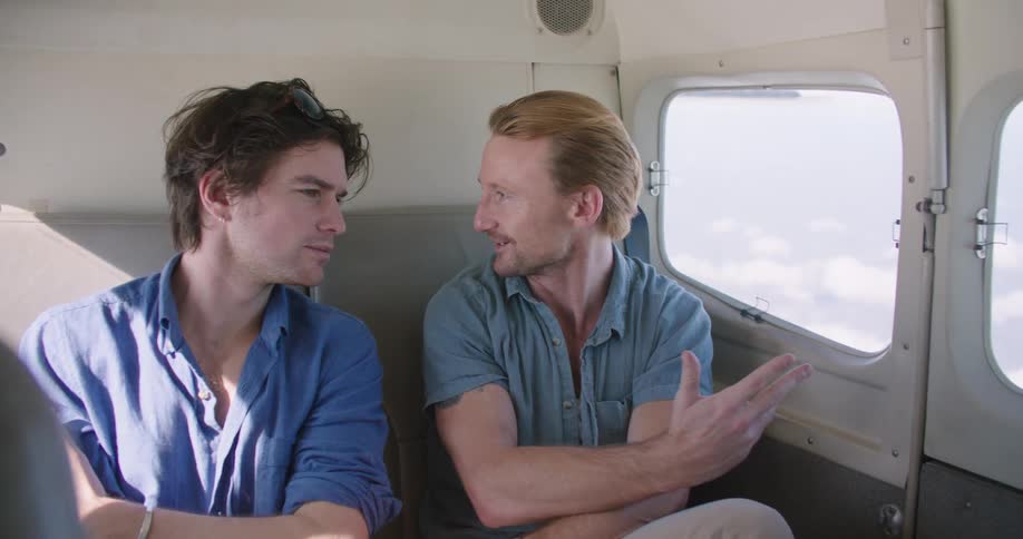 Two young sitting on a small airplane talking and looking out the window