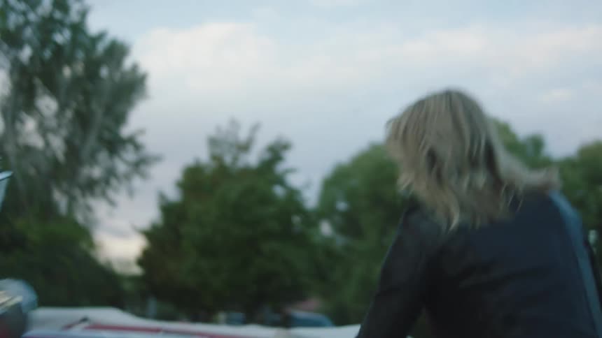Blonde woman and red haired bearded man sit on curb near bridge drinking soft drinks before rushing to car and driving away