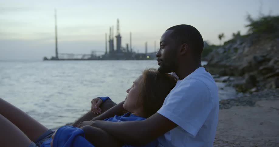 A young couple are relaxing in each others embrace while sitting on a lake shore at dusk