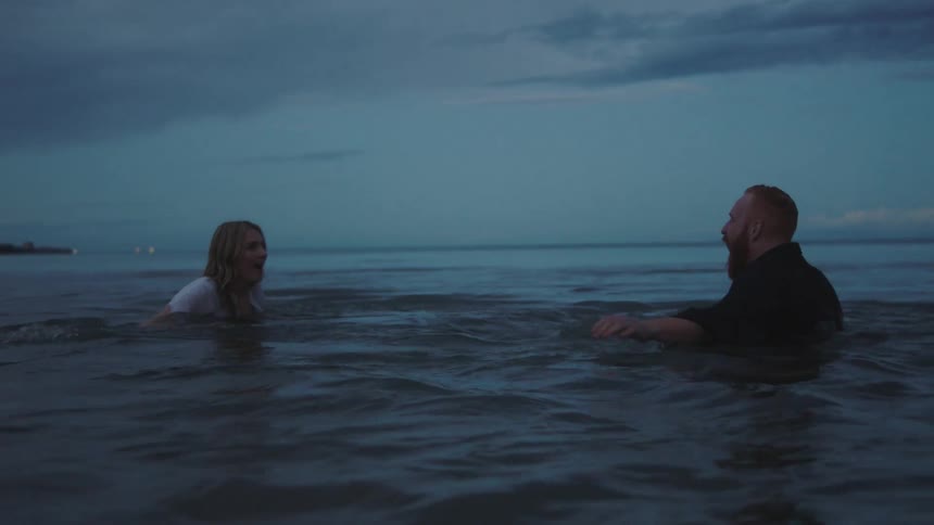 A man and woman are wading and swimming in a lake in their clothing at night