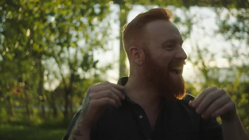 Man with red beard and black shirt with blonde woman wearing black leather jacket sits on sidewalk and play with each other in the street at sunset