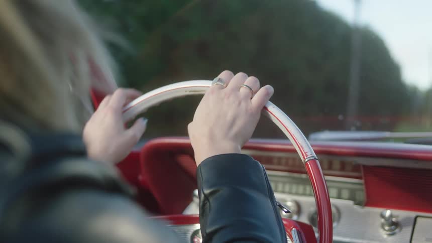 A woman has her hands on the steering wheel and is driving a vintage convertible car