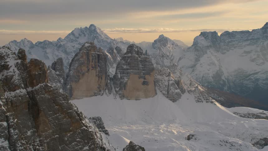 A pair of tall rock formation atop a snow covered mountain on a cloudy evening