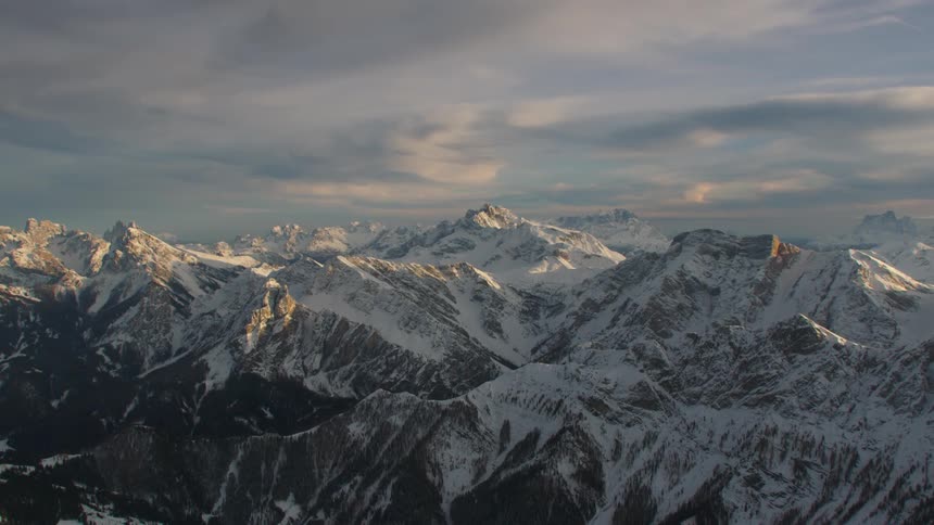 A range of snow capped mountains under a cloudy evening sky