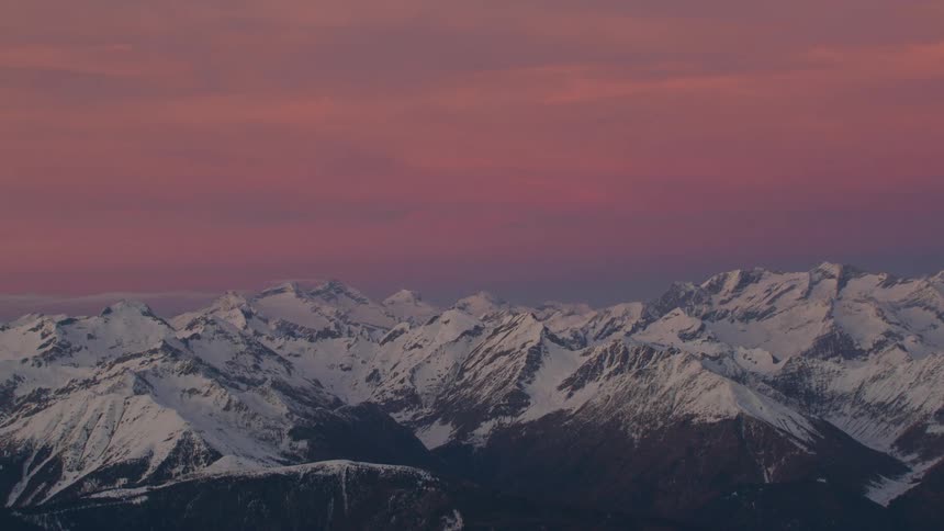 Mist covers snowy mountain range under red sky