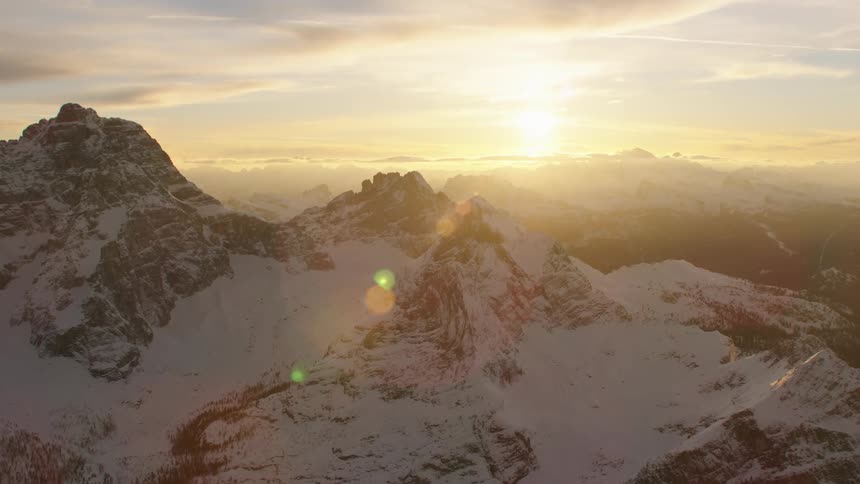 The sun shines on a snow covered mountain range during the day