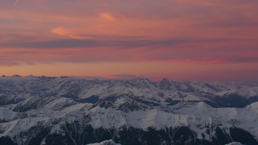 Snow covered mountains stretch to horizon under red sky on misty day