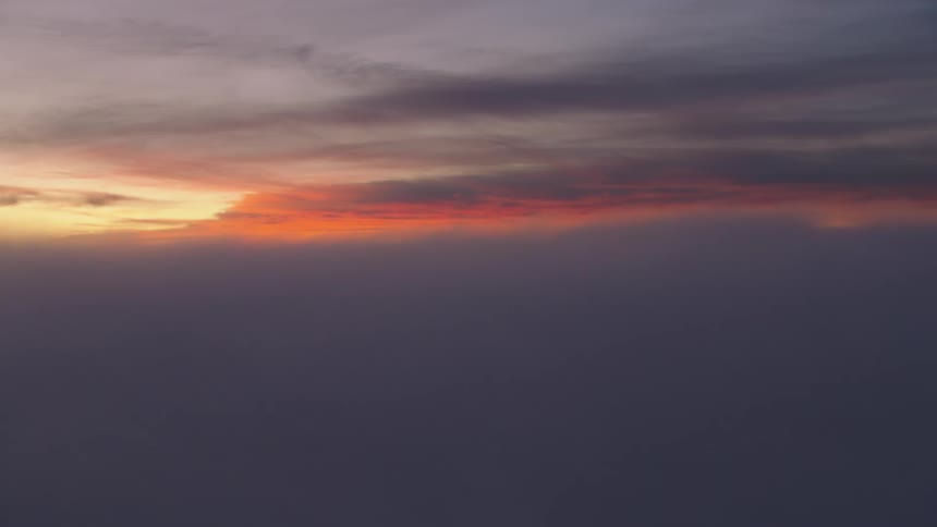 Thick clouds loom over a snowy mountain range at sunset