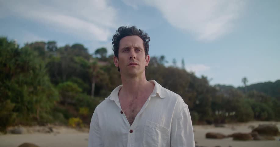 Man with white shirt stands on the beach watches the sea thinking