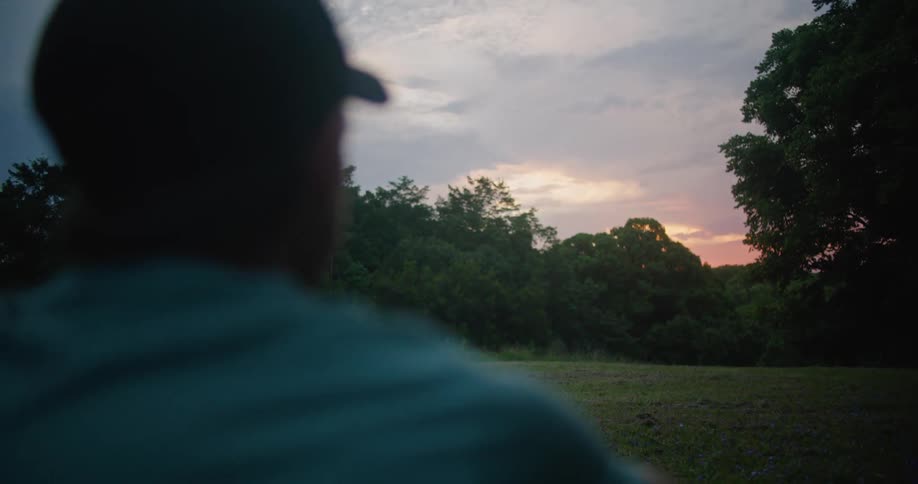 A man is standing and looking over a large grassy area surrounded by trees
