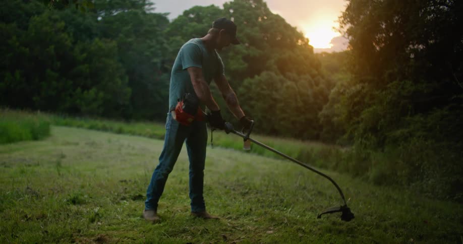 A man swings the trimmer across the field of grass