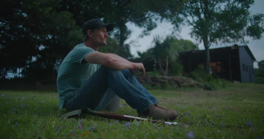 A man sits in the grass by a shovel